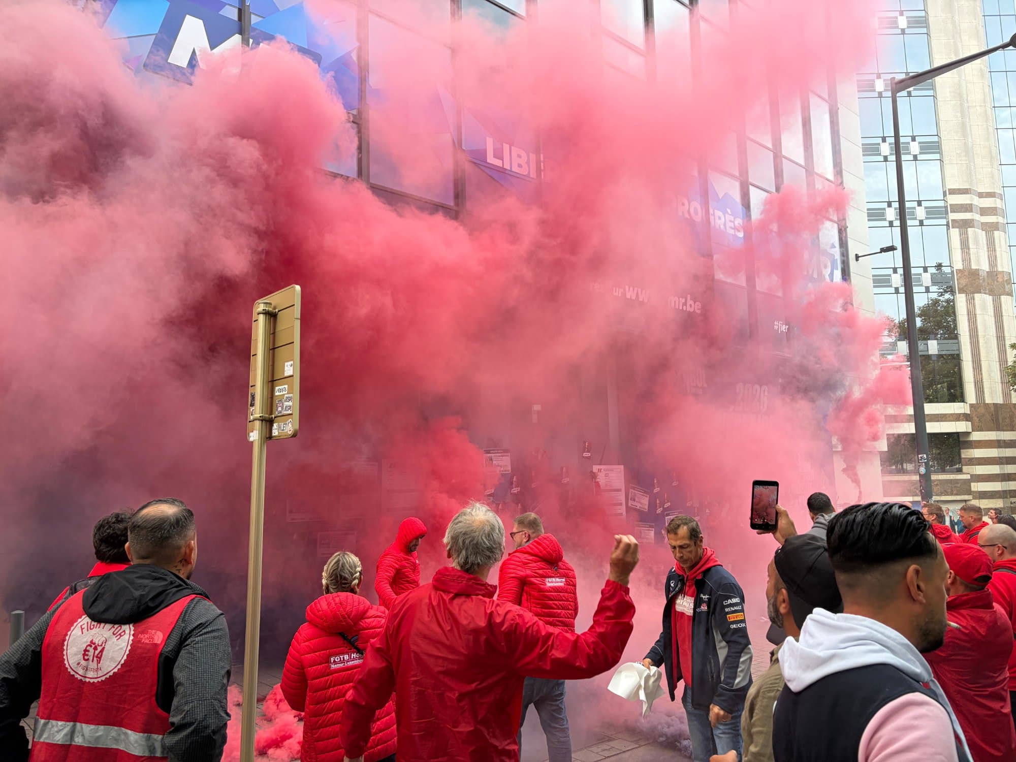 Militants en veste rouge, l'un d'eux lève le poing dans la fumée des fumigènes.